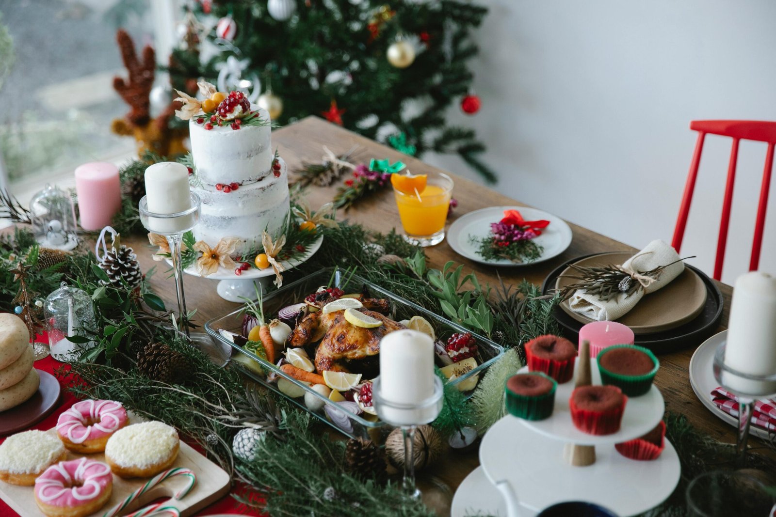 Festive Christmas dinner table with a decorated cake, roasted chicken, cupcakes, and greenery