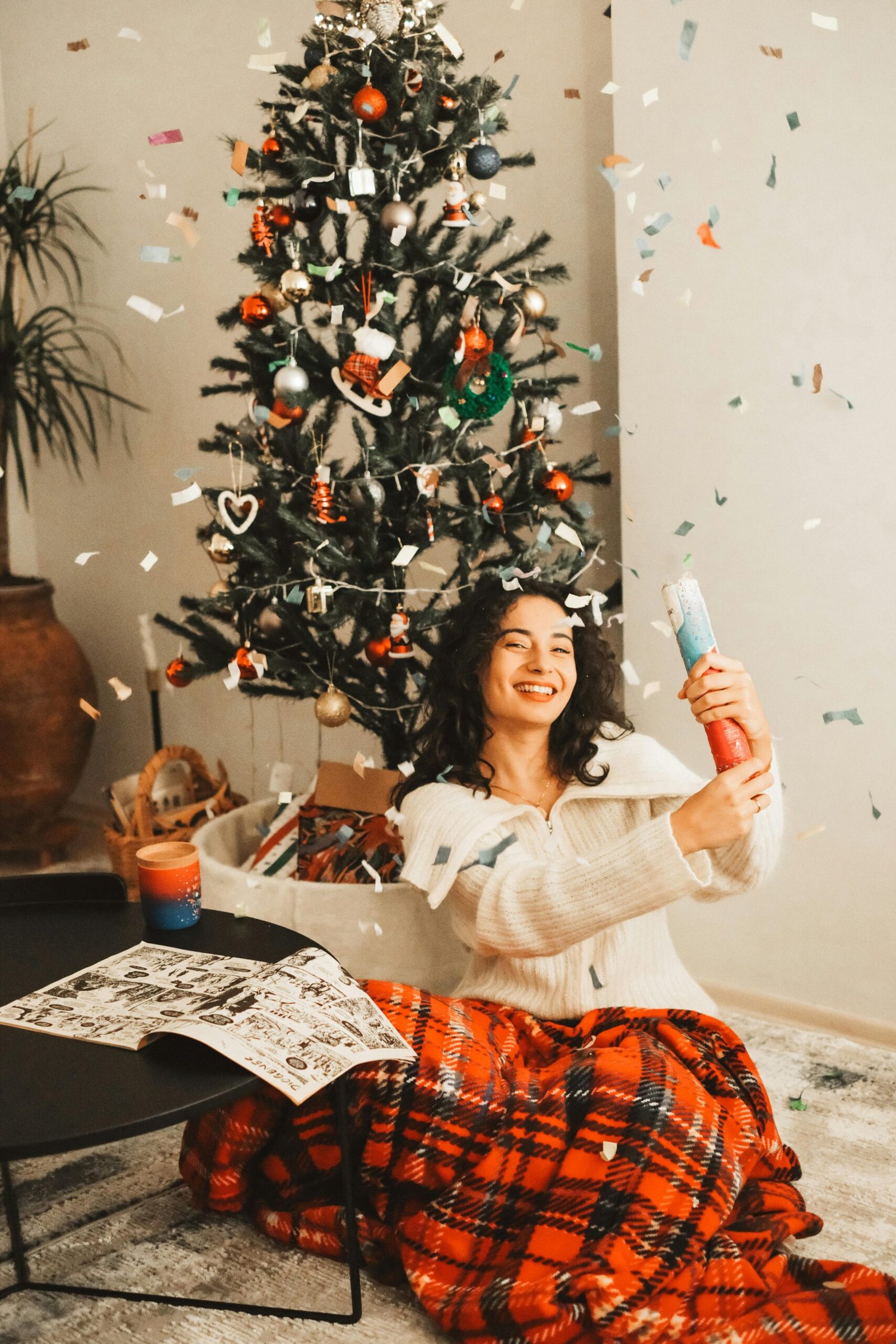 Woman celebrating Christmas with a confetti popper by a decorated tree